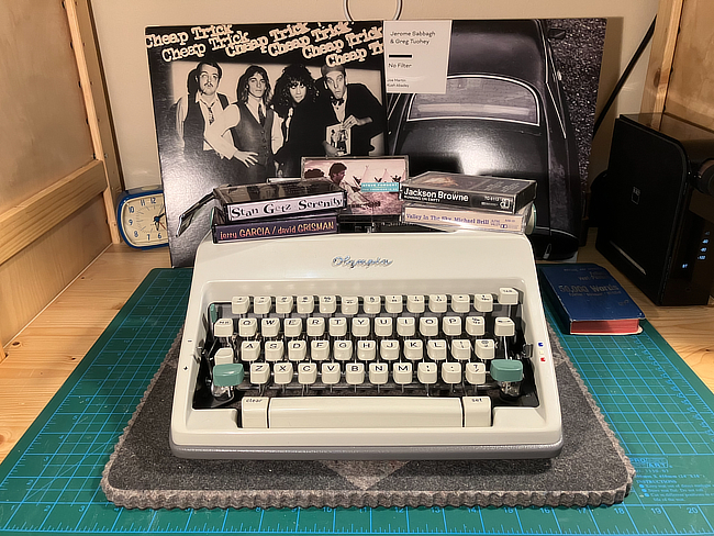 A typewriter surrounded by vinyl records and cassettes.