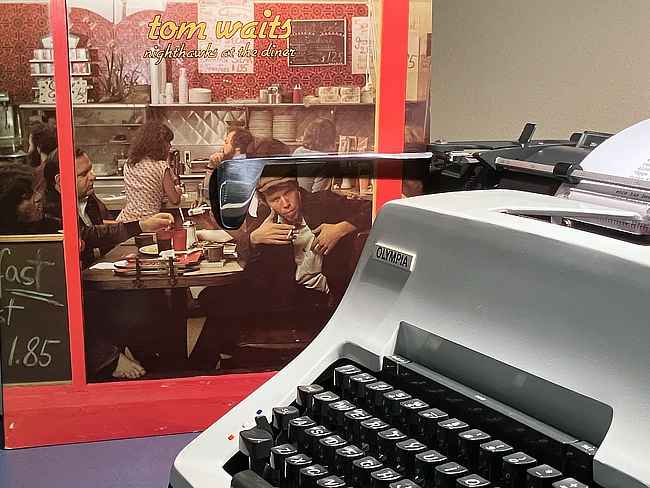 A copy of Tom Waits' LP "Nighthawks at the Diner" sits next to an Olympia SG3 typewriter.