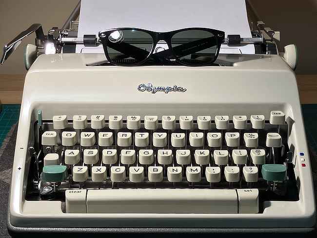 A pair of black RayBan sunglasses sitting on top of an Olympia SM9 typewriter